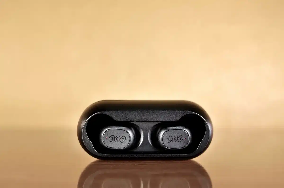 Three different earbuds and headphone models arranged on a clean white surface, each representing a different form factor, with subtle shadows and depth of field, cool neutral lighting