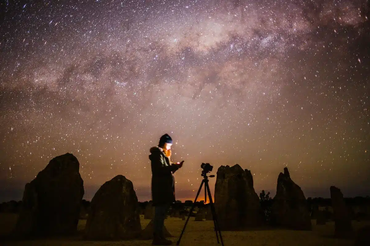 Smartphone mounted on sturdy tripod in dark environment, long exposure setup ready for night capture, timer visible on screen