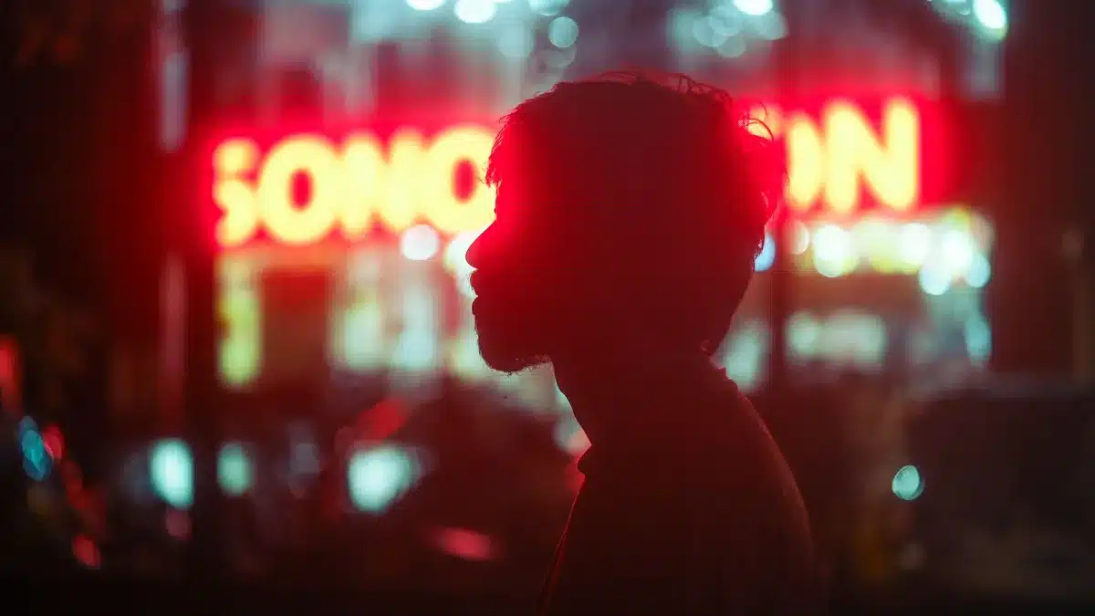 Night urban scene with neon signs and streetlights creating ambient light, smartphone in foreground capturing the scene