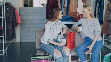 Manos de cliente examinando vaqueros doblados en estantería de outlet con etiquetas de precio