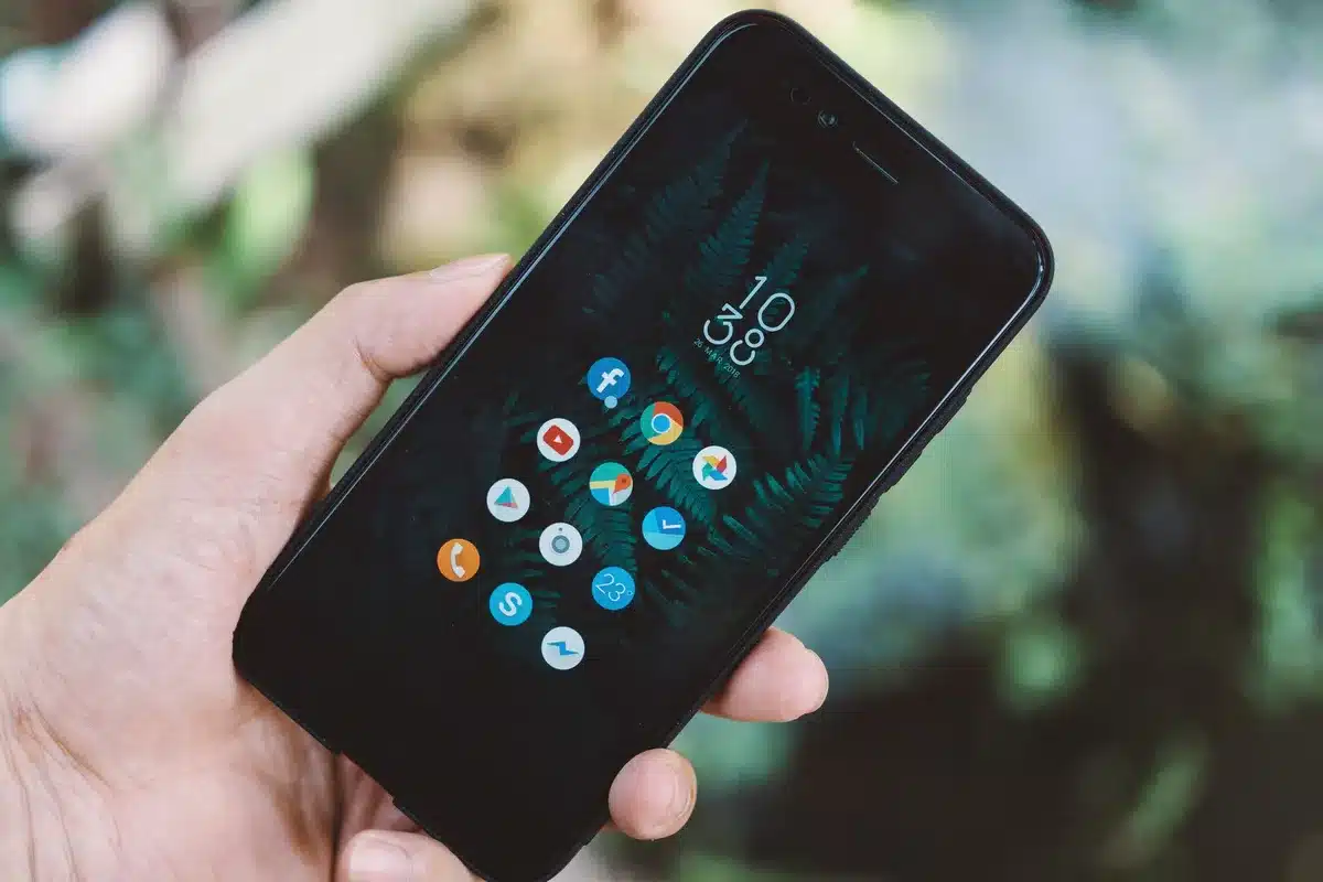 Manos sosteniendo un smartphone con pantalla AMOLED mostrando aplicaciones y contenido multimedia