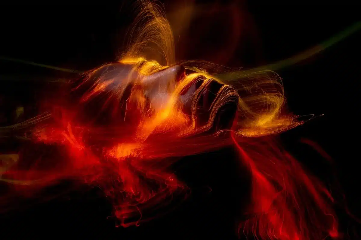 Líneas luminosas abstractas dibujadas en la oscuridad con una linterna, trazos de color suave contra fondo negro, modo Bulb