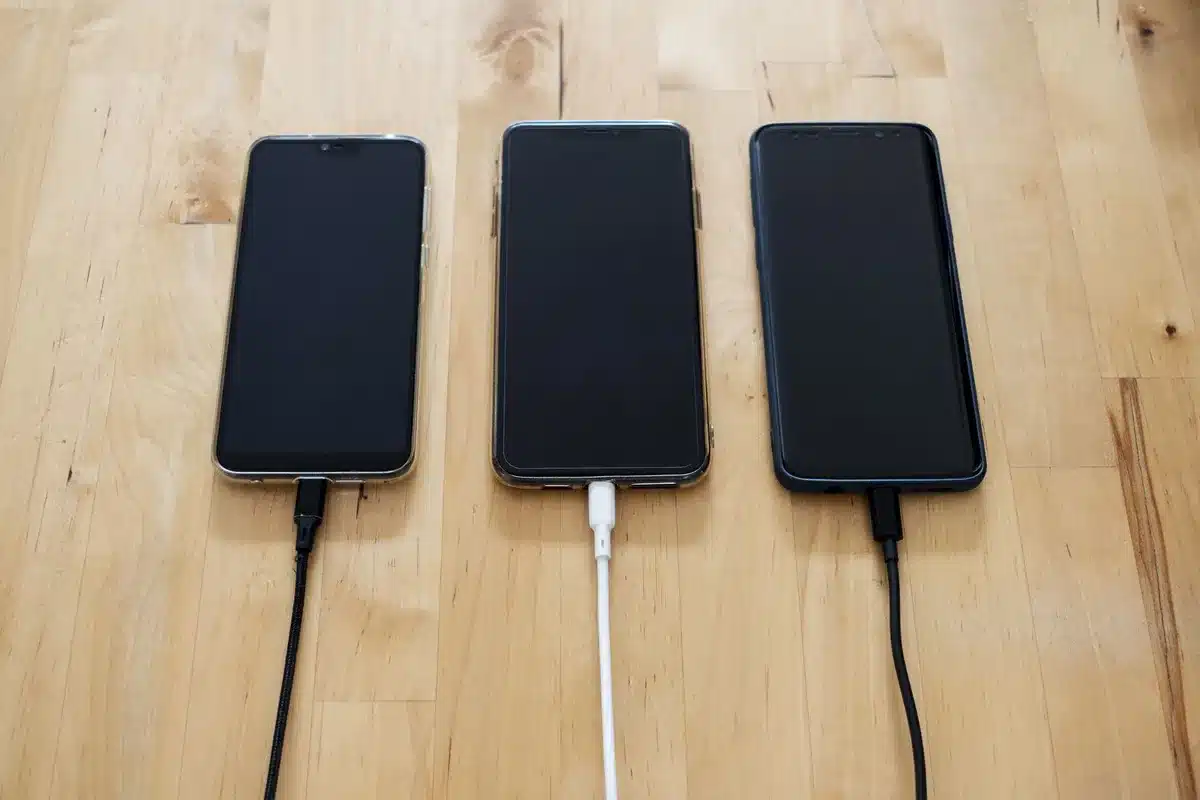 empty desk with an unbranded large smartphone face-up, charging cable nearby, soft daylight through a window