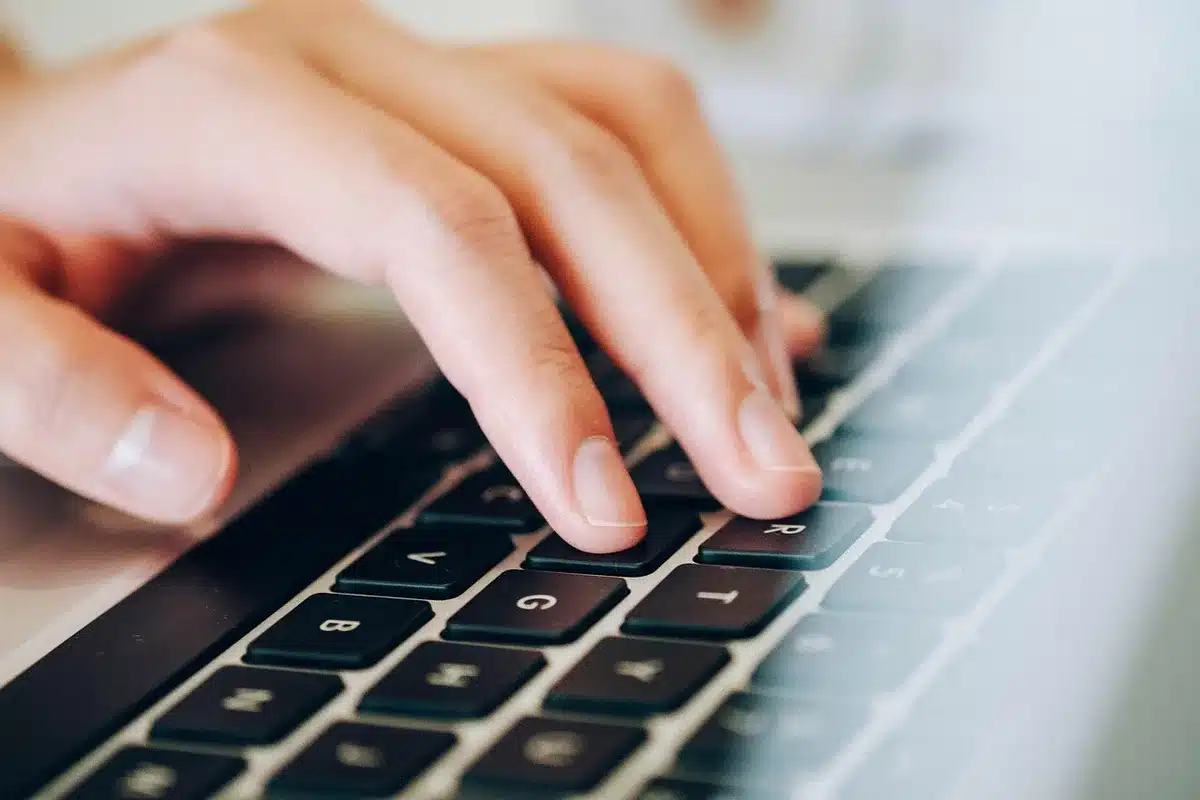 Close-up of an open notebook, a cup of coffee and an anonymous pair of hands typing on an unbranded laptop keyboard, soft indoor light