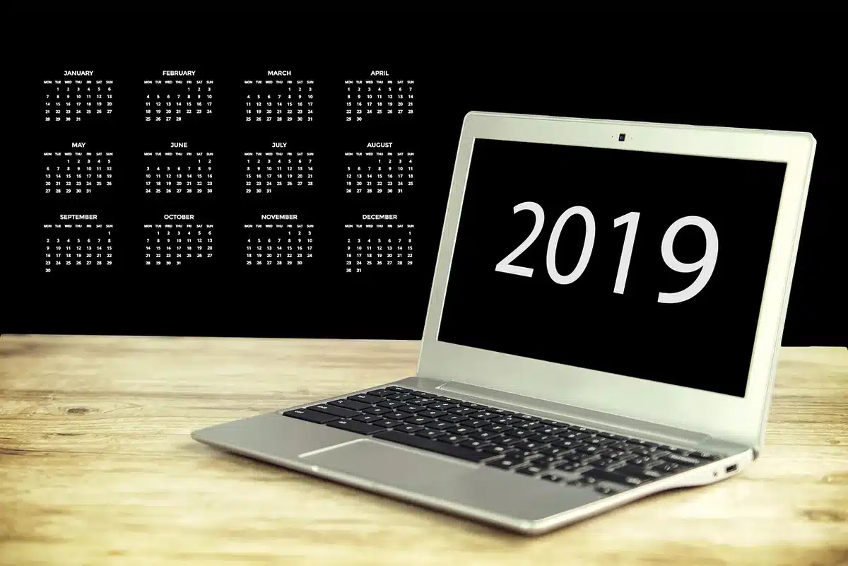 Close-up of an anonymous laptop keyboard with a small sticky note reading only dots, and a generic calendar app window blurred on the screen