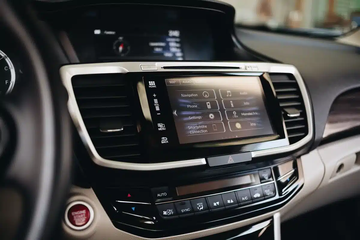 Close-up of an anonymous steering wheel with infotainment screen blurred in background, smartphone cable coiled on dash, no brand visible