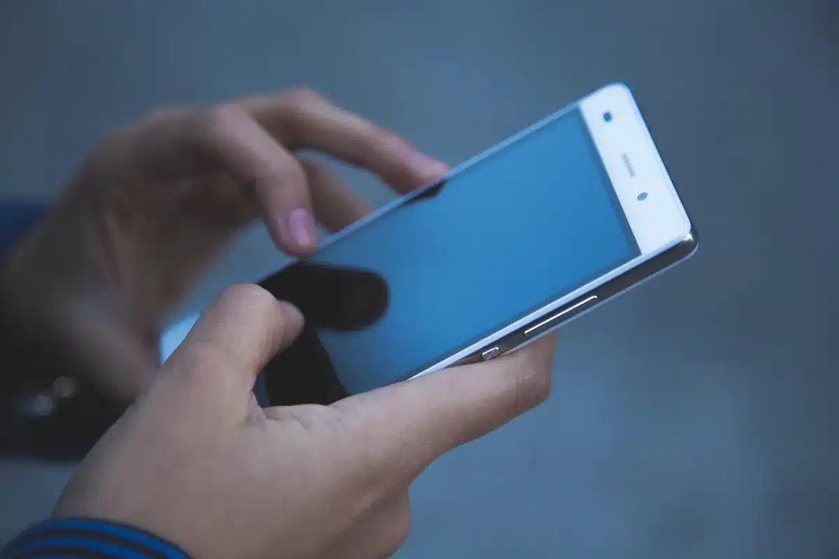An empty smartphone on a kitchen table with a visible WhatsApp chat list blurred on screen, a small handwritten note nearby that reads nothing legible — evokes a domestic fraud scene