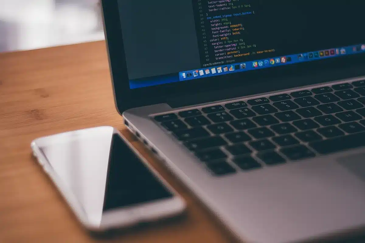 empty modern workspace with an anonymous person’s hands typing on a laptop showing anonymized code snippets on screen