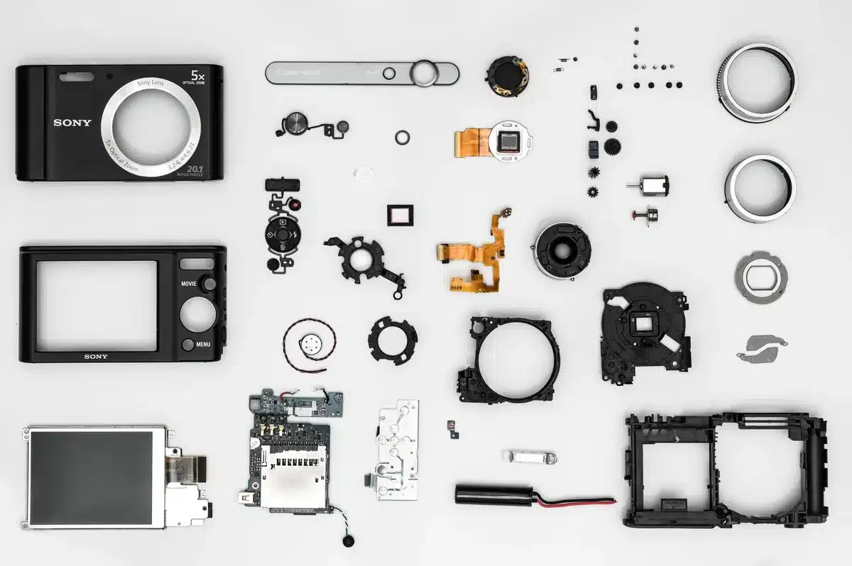 Anonymous hands holding a blank camera lens housing next to an unbranded smartphone on a workbench, tools blurred in background
