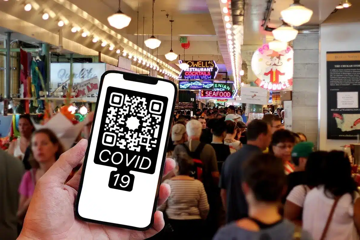 A close-up of an anonymous hand holding a smartphone showing a blurred QR code on screen, a second hand pointing to it; no brands or text visible