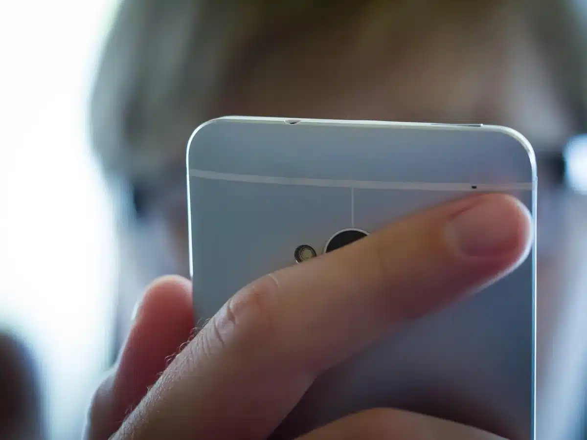 An anonymous pair of hands holding an unbranded phone while a finger long-presses the lock screen to enter customization, with blurred kitchen background; faces not visible.