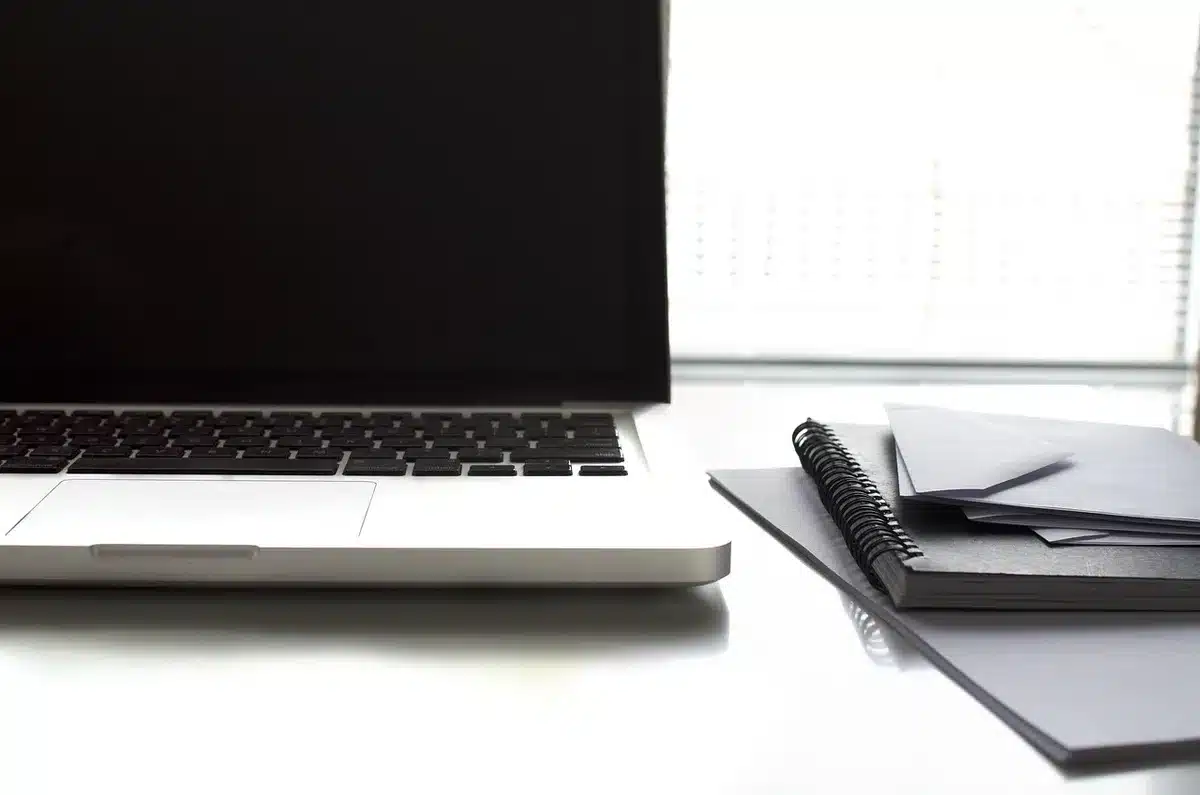 Empty modern office desk with a closed laptop and a dim monitor showing a black screen, a keyboard and a touchpad in soft focus