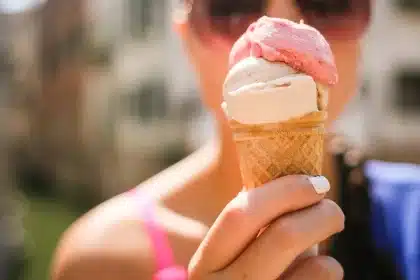 Manos tomando crema de un envase azul sobre una repisa de baño con toallas