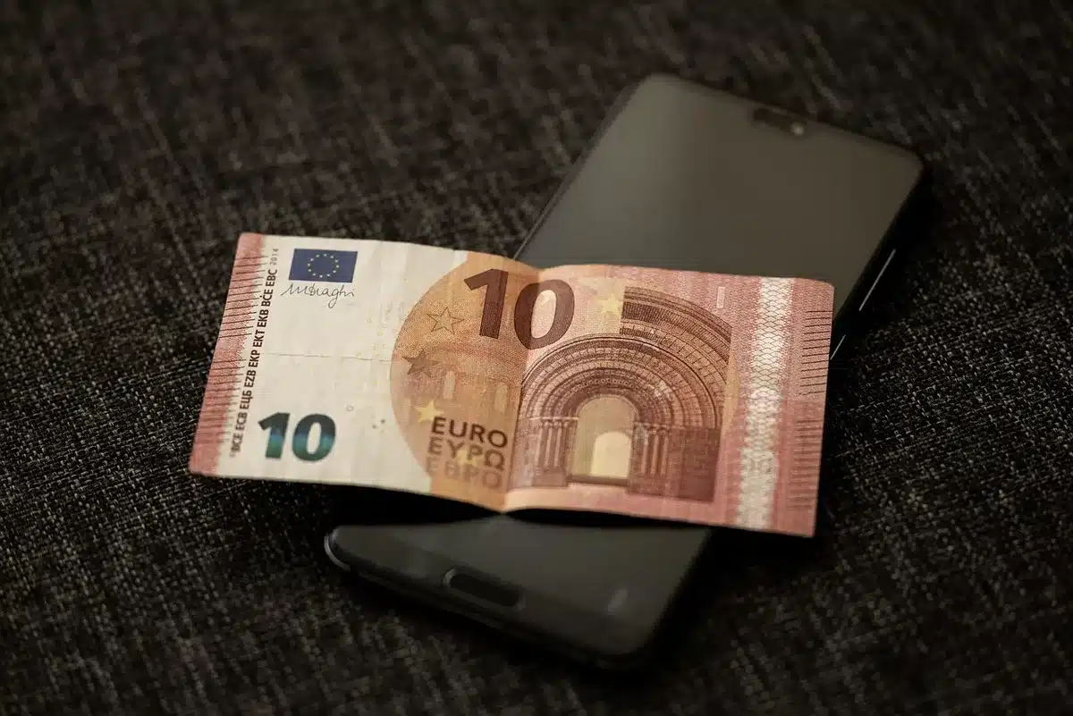 anonymous hands holding a smartphone showing a blurred screen, with a blurred office background suggesting remote work and finance