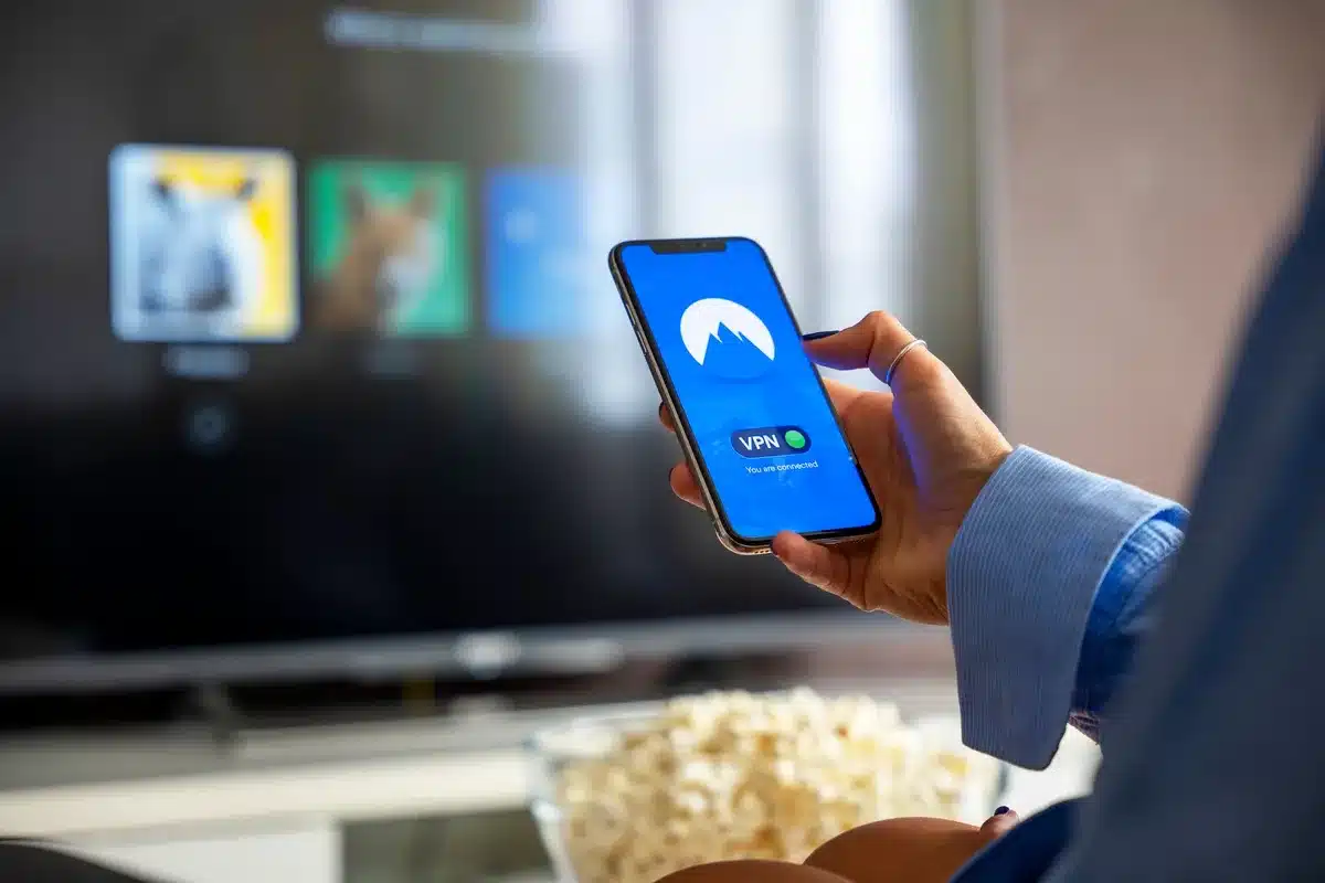 Two anonymous hands holding a remote and a smartphone showing a streaming app interface