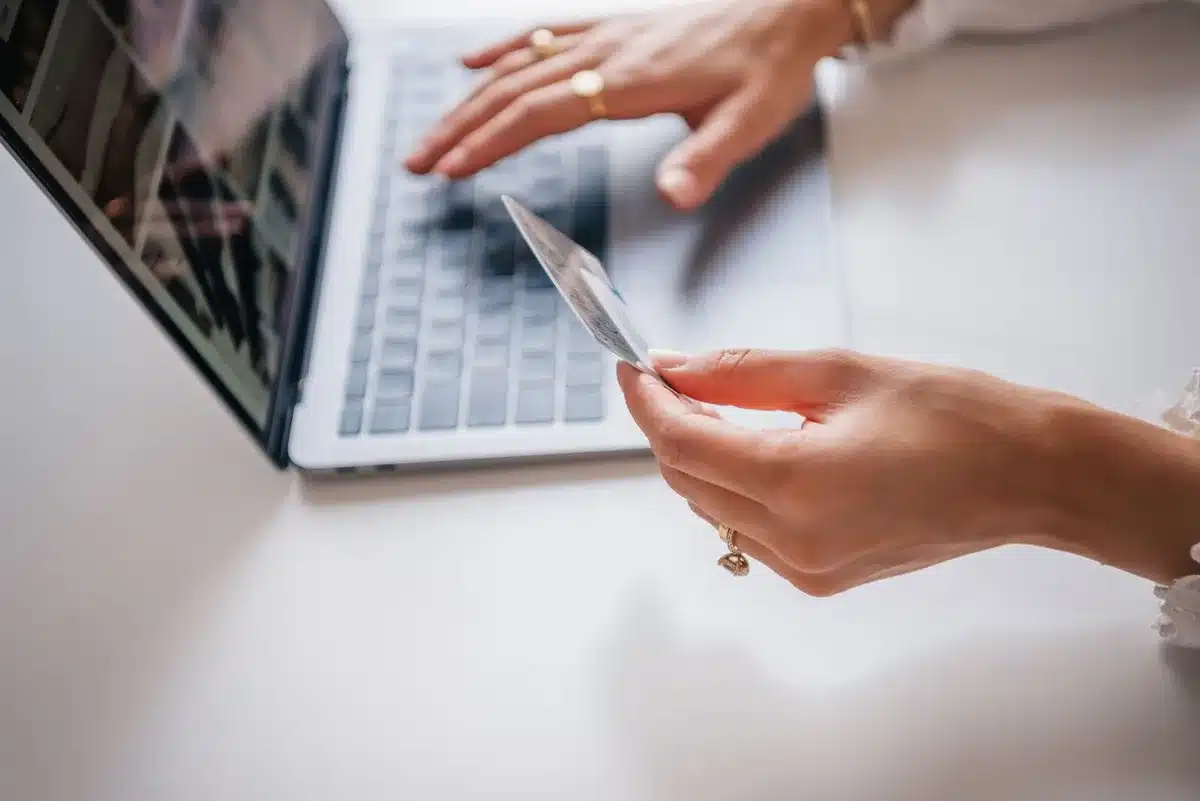 anonymous hands holding a generic smartphone above a laptop with shopping page blurred