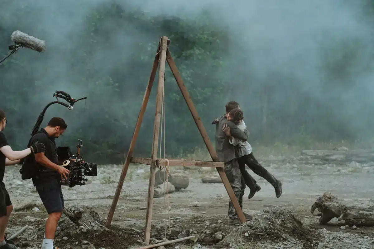 Long shot of an anonymous film set with lighting rigs and a clapperboard left on a table, crew silhouettes blurred