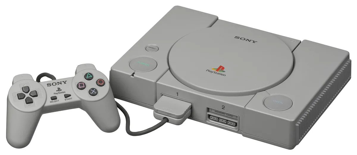 A black unbranded console silhouette resting on a low table, a soft glow from a TV screen behind it, no logos visible, solitary and tidy living-room setting