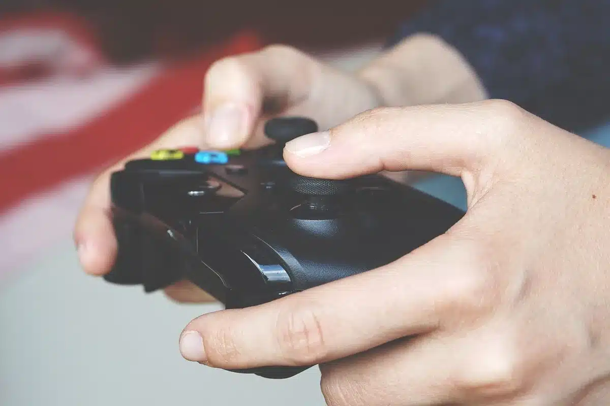 An anonymous person silhouetted against a TV, hands on a controller, dark room with soft backlight, no identifiable face or logos